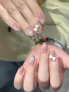 Close-up detail of short oval nude press-on nails with 3D bows and cute cat designs.