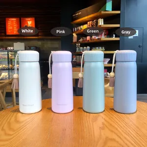 Four colorful insulated water bottles with tassel accents in a cafe setting