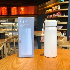 White vacuum flask with tassel charm shown with original gift box in a cozy cafe