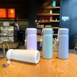 Details of colorful insulated bottles with decorative tassels on a wooden cafe table