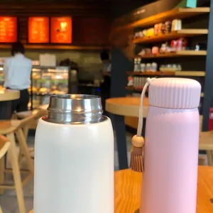 Close-up of a pink thermos with a decorative tassel and a white wide-mouth cup
