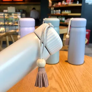 Close-up of pastel insulated water bottle with decorative tassel charm in a cafe