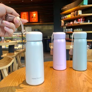 Pastel insulated water bottles with stylish tassels shown in a cozy cafe setting.