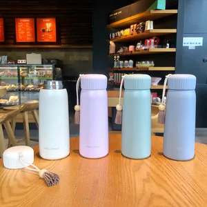 Group of pastel insulated water bottles with stylish tassels in a cozy cafe setting.