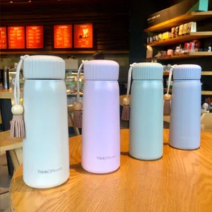 Pastel insulated water bottles with tassels and wooden beads in a cozy cafe setting