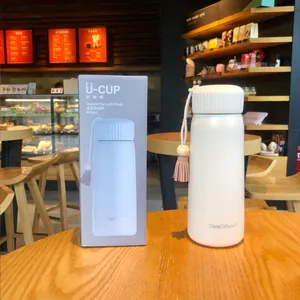 Close-up of a white vacuum flask with a decorative tassel and its grey packaging box.