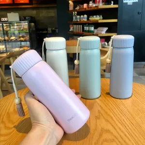 Close-up of a pink insulated water bottle with a cute tassel strap in a cafe