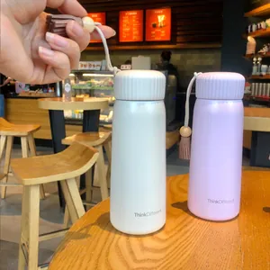 Elegant insulated water bottles with tassel handles in a cozy cafe setting.