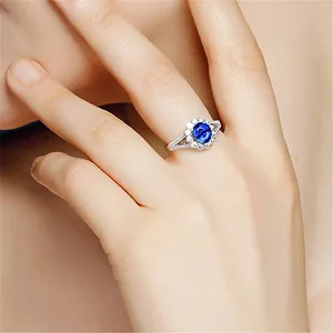 Close-up detail of silver halo ring with a vibrant blue oval center stone on finger