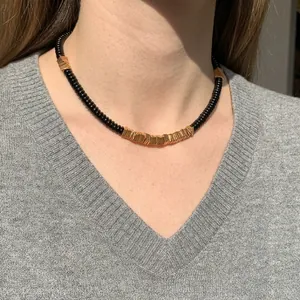 Natural black coconut shell and gold copper alloy beaded necklace worn on a model's neck