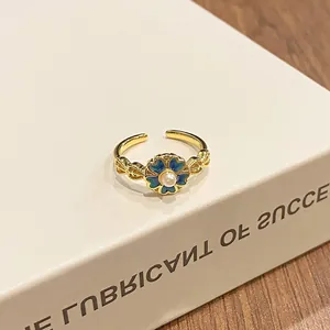 Macro detail of a vintage gold floral open ring with gradient blue enamel and a white pearl.