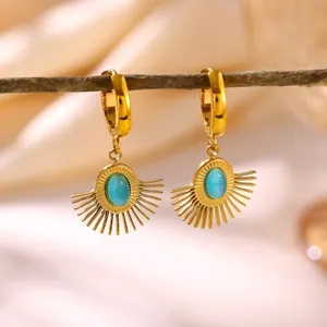 Close-up of gold sunburst hoop earrings with a turquoise oval center stone displayed on a branch