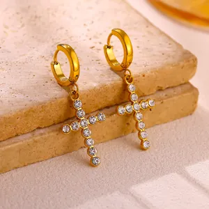Detail of gold stainless steel hoop earrings featuring crystal-studded cross pendants.