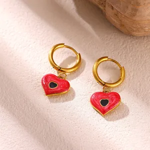 Detail view of red heart-shaped drip oil earrings with gold stainless steel hoops.