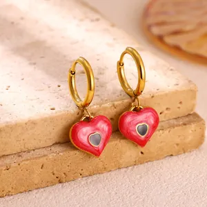 Close-up of red enamel heart-shaped earrings on a natural stone block.