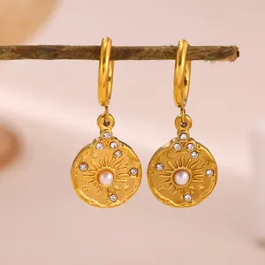 Close-up of gold sunburst drop earrings with central pearl and rhinestone accents.