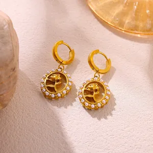 Close-up of golden stainless steel rose earrings with delicate pearl trim on a warm background.