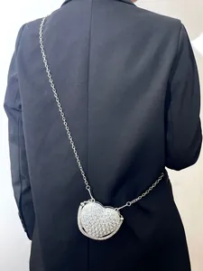 Vue détaillée d'un mini sac chaîne en forme de cœur en strass porté sur un blazer noir.