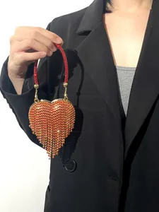 Détail du sac de soirée cœur en strass rouge avec pompons élégants tenu par le mannequin.