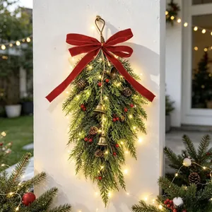 Detailed view of festive Christmas teardrop swag with red velvet bow, golden bells and warm LEDs