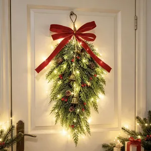 Festive Christmas teardrop wreath with bells and warm LED lights on a white door