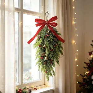 Christmas teardrop swag with evergreen branches, red berries, and golden bells on a window