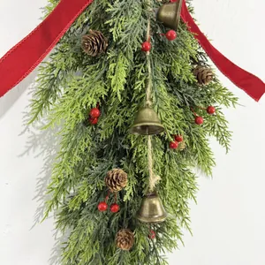 Detailed view of a Christmas wall swag with golden bells, pine cones, and red berries.