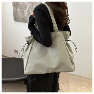 Close-up view of a minimalist sage green drawstring tote bag worn by a model in a studio