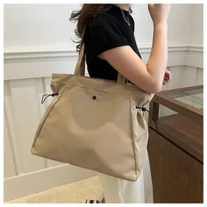 Detailed side view of a large khaki canvas tote bag worn by a model in a bright room.