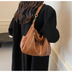 Detail of a retro brown leather tote bag worn as a shoulder bag on a warm black coat