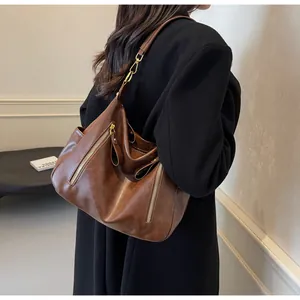 Detail view of a vintage brown leather tote bag worn by a model in a black coat