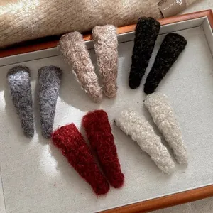 Close-up of fuzzy lamb wool hair clips in various colors displayed in a wooden tray