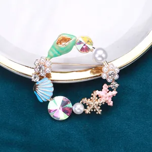 Detailansicht einer Emaille-Brosche im Meeresdesign mit Seesternen und Perlen.