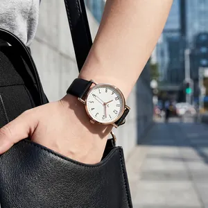 Close-up of a minimalist women's quartz watch with a black litchi leather strap on wrist