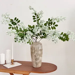 Detailansicht realistischer weißer Schnurbaumblüten in einer beigen Vase auf einem Tisch
