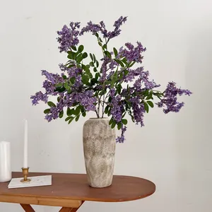 Elegante lila künstliche Akazienblüten in einer Steinvase auf einem Holztisch.