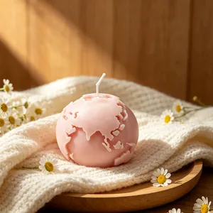 Cozy pink 3D Earth shaped scented candle on white knit fabric with small white daisies