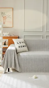 Detalle de una manta para sofá gris claro con diseño de espiga y flecos en un salón