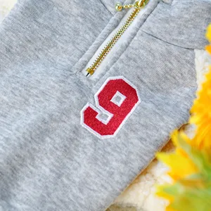 Close-up detail of grey pet warm jacket with gold zipper and embroidered number 9