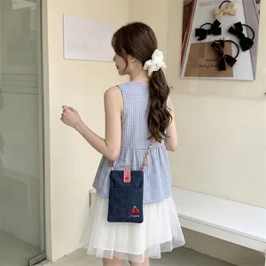 Small denim crossbody bag with cherry embroidery worn by a model in a casual style