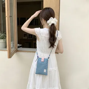 Detailed view of a cute embroidered denim mini crossbody bag worn by a model in a white dress