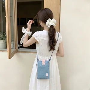 Close-up of cute bunny embroidery on denim crossbody bag worn by model in white dress