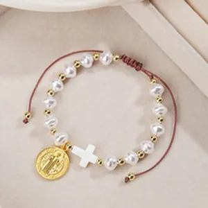 Dettaglio di un bracciale di perle artigianale con croce bianca e pendente dorato