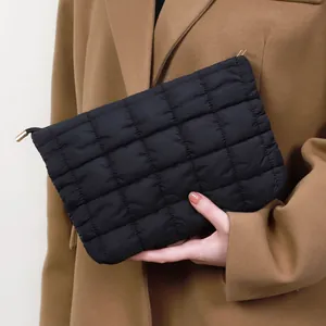 Trousse cosmétique matelassée noire élégante tenue par un mannequin en manteau camel.
