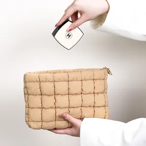 Trousse à maquillage matelassée beige élégante tenue par un mannequin en blazer blanc