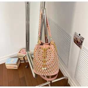 Dettaglio di una borsa a secchiello rosa stile punk con borchie, strass e catena dorata.