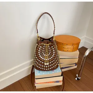 Dettaglio borsa a secchiello marrone stile punk con strass e borchie su una pila di libri