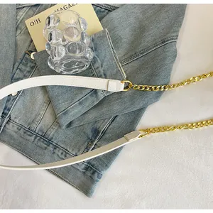 Dettaglio della catena dorata e della tracolla in pelle bianca di una borsa a mano stile punk