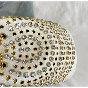 Dettaglio di borsa in pelle bianca con occhielli dorati e borchie di strass brillanti
