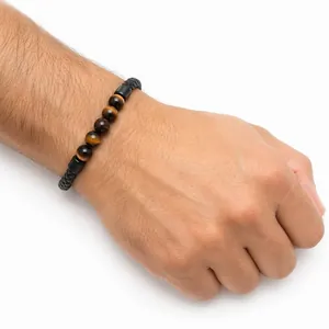 Primo piano di perle in occhio di tigre da 6 mm su un bracciale in pelle intrecciata nera da uomo.